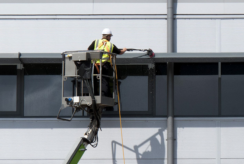Man in a cherry picker power washing the side of a building